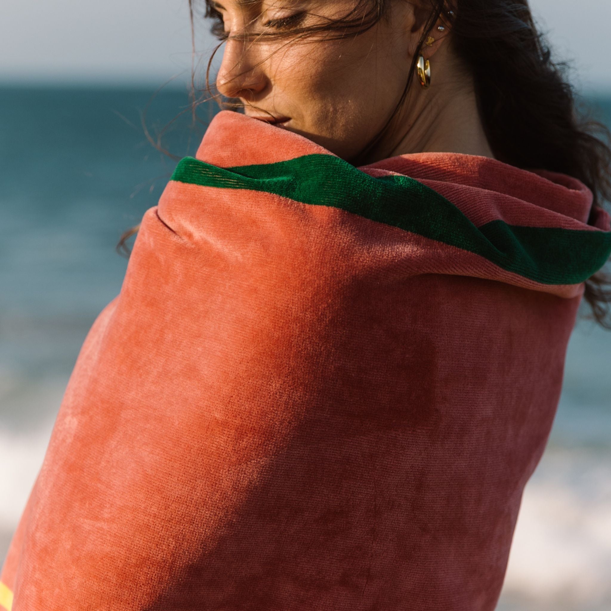 Woman wrapped in a cognac beach towel with green stripe on a beach