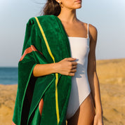 Woman in a white swimsuit holding a green beach towel on a beach