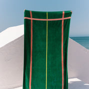 Green towel with cognac stripes draped over a white wall with ocean view