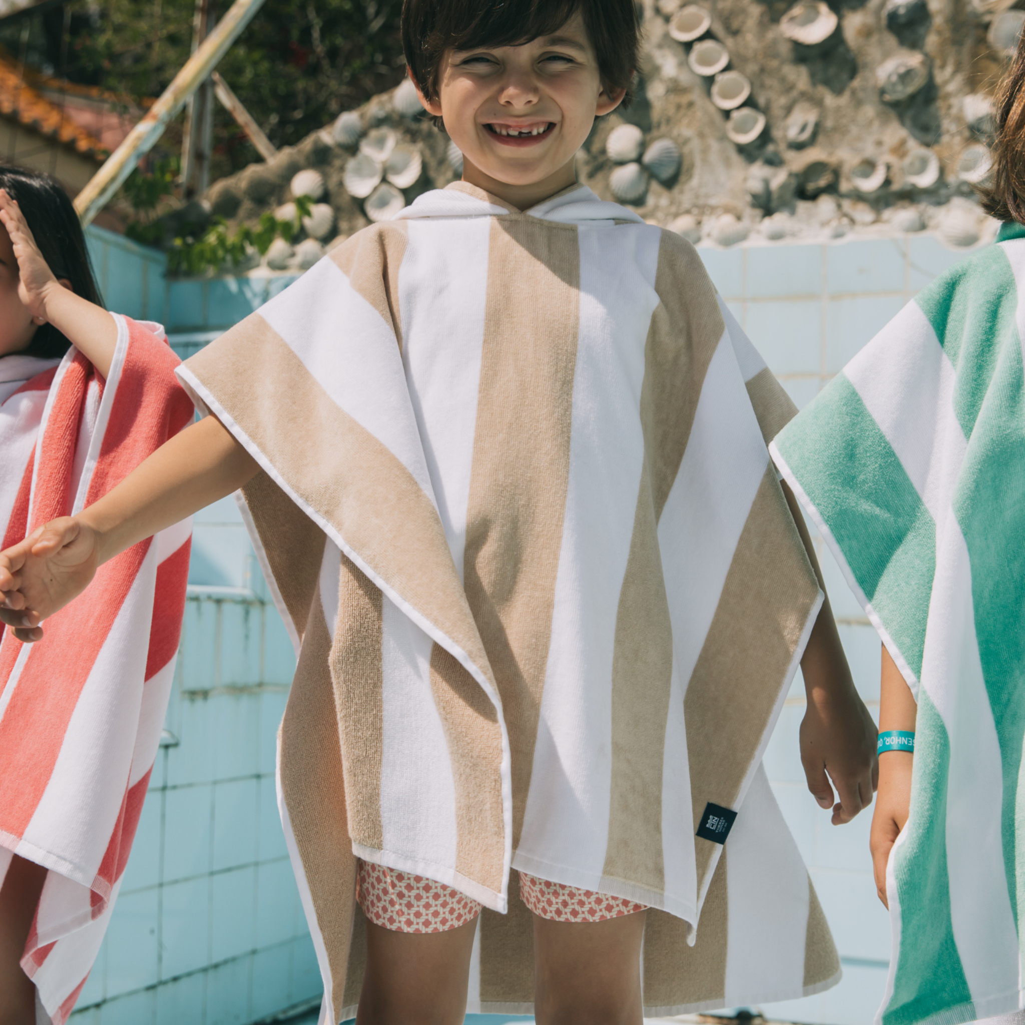 Child wearing a striped poncho with a pool in the background