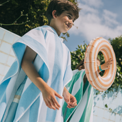 Kid wrapped in a striped poncho with a pool float, outdoors on a sunny day.