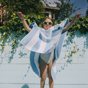 Kid with a blue and white striped poncho draped over their shoulders by a pool.