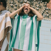 Kid wearing a green and white striped poncho with a shell-patterned wall in the background