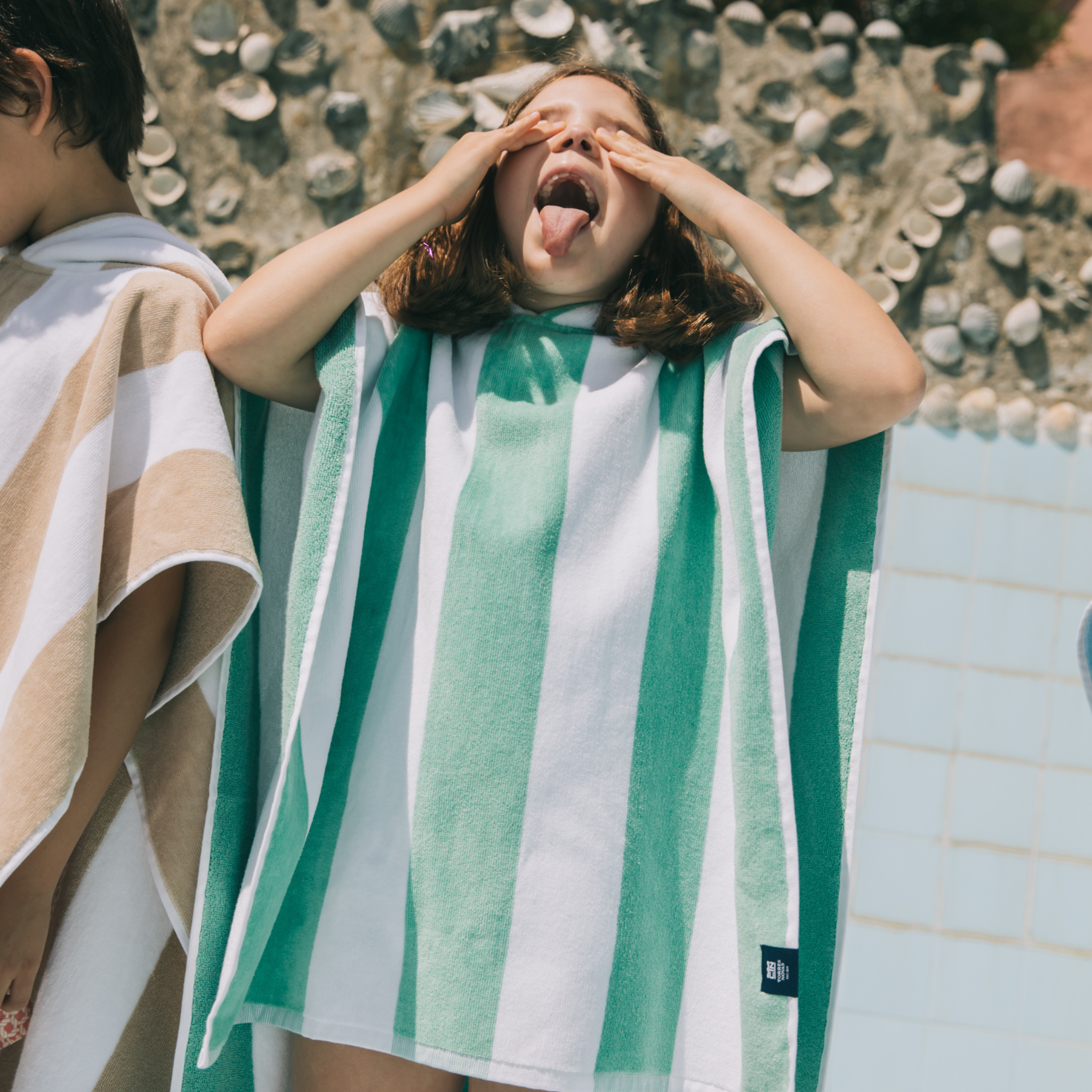 Kid wearing a green and white striped poncho with a shell-patterned wall in the background