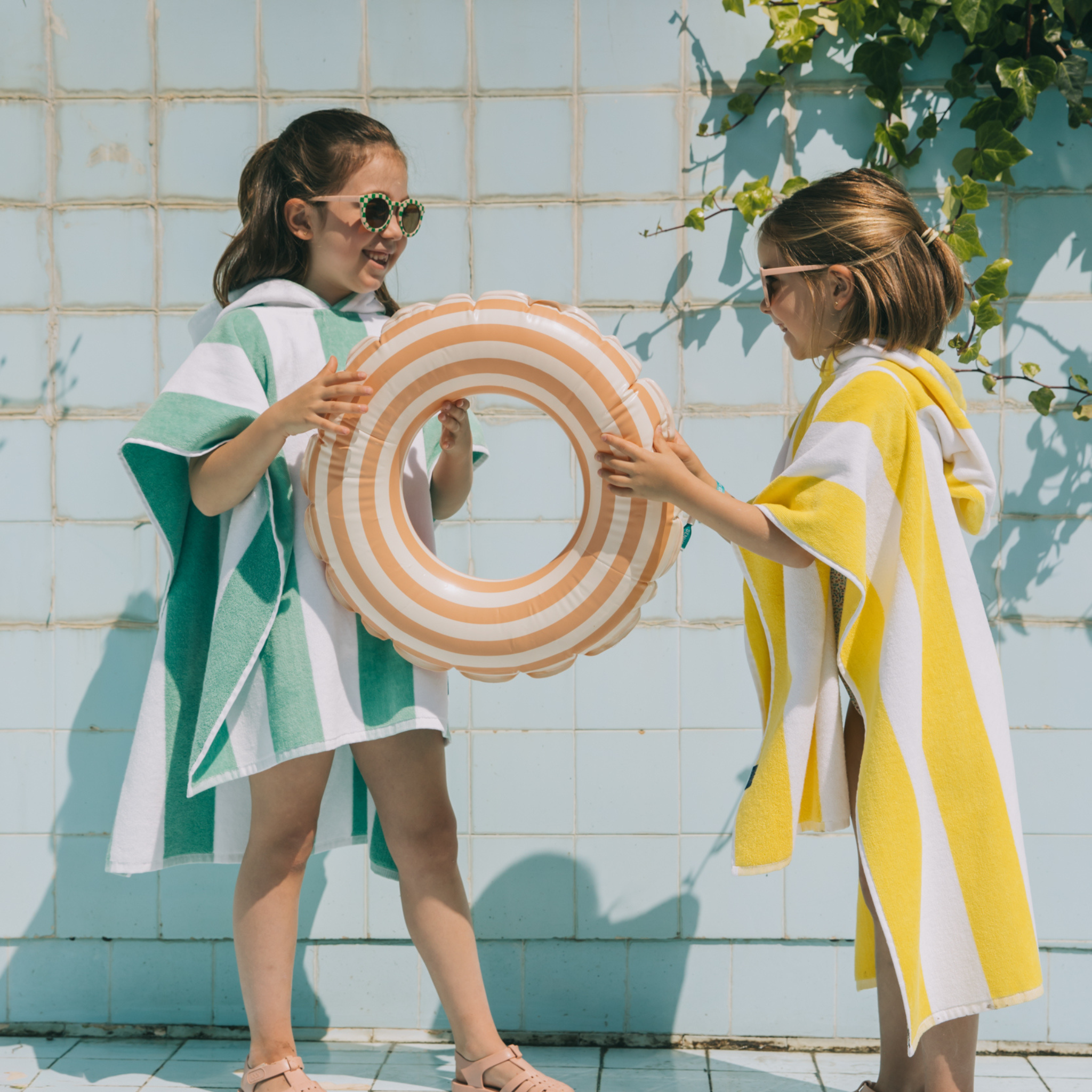 Two kids holding a striped inflatable ring against a tiled wall.