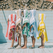 Children wearing colorful hooded ponchos by a poolside.