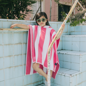 Kid wearing a pink and white striped poncho leaning against a tiled wall.