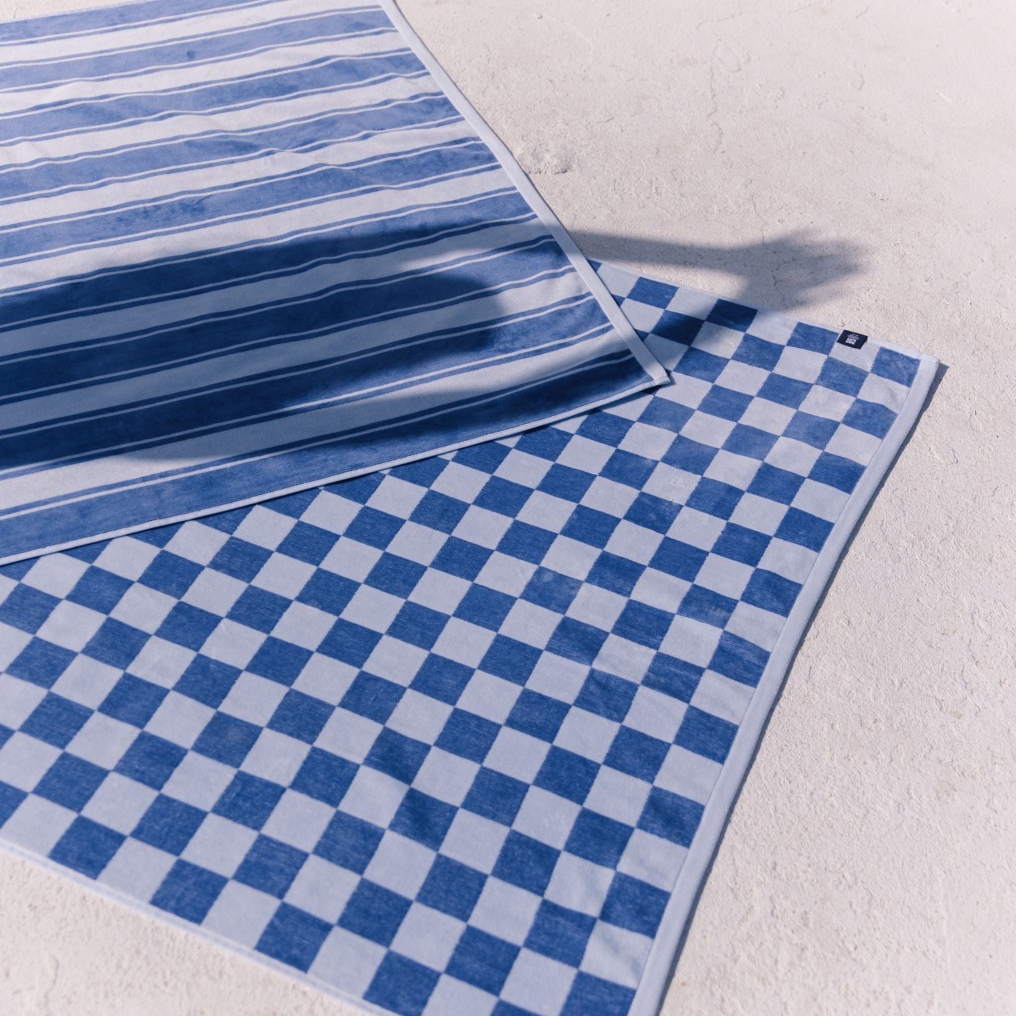 Two blue patterned beach towels on a light gray surface