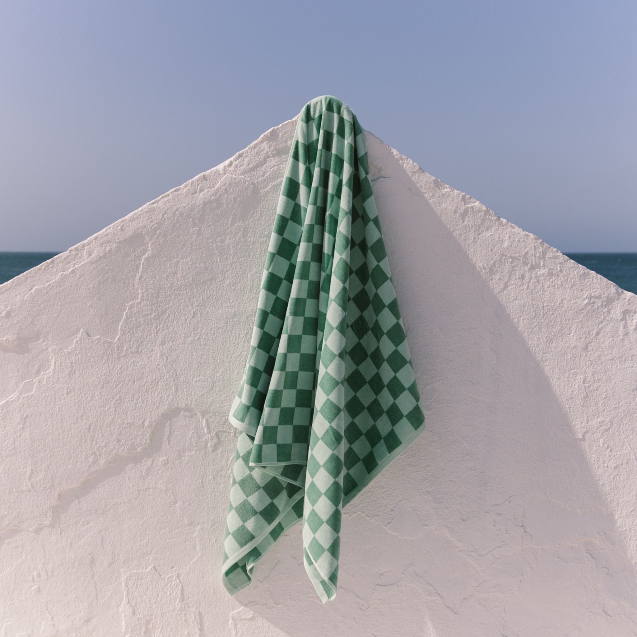 Green checkered beach towel draped over a white wall with a blue sky background