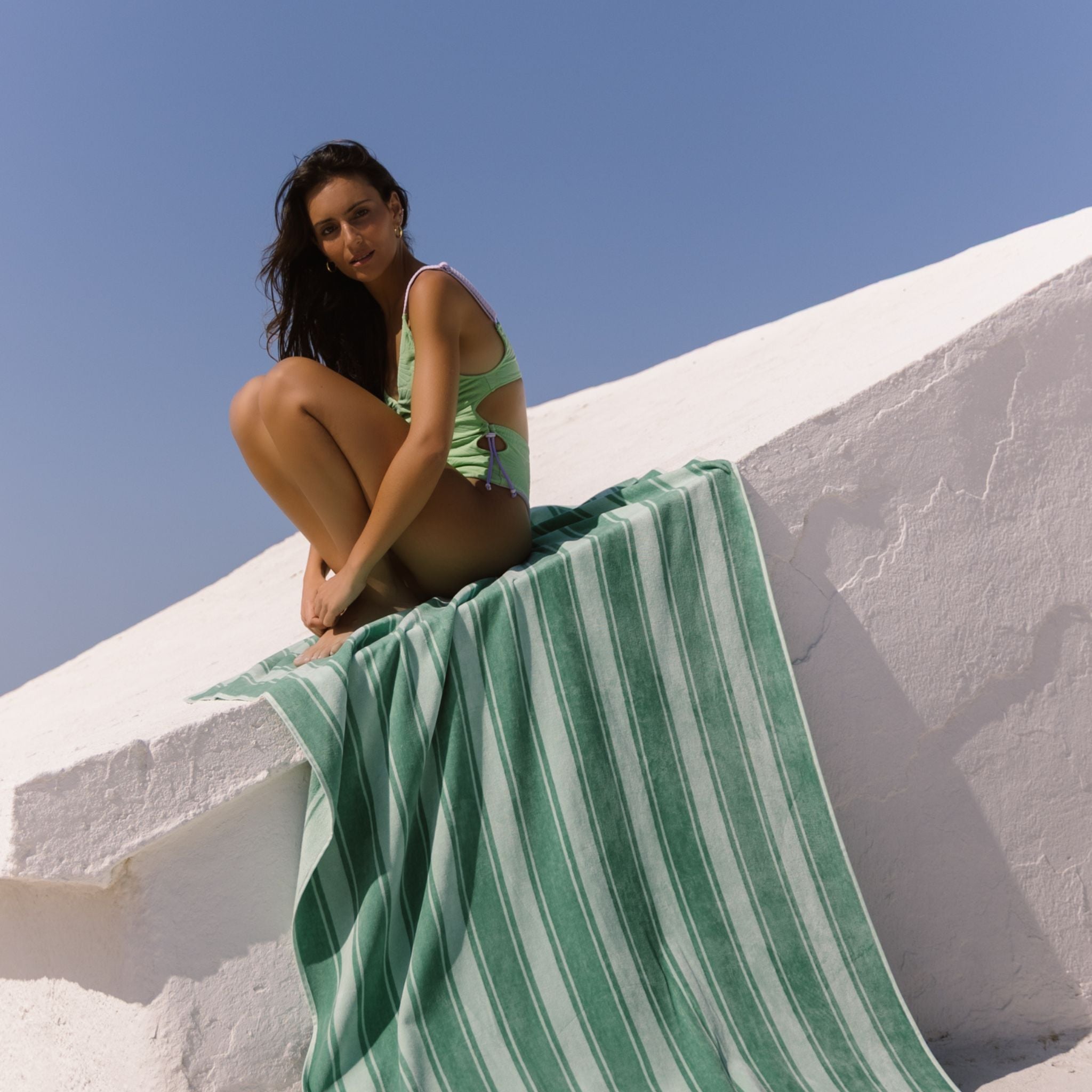 Woman sitting on a white ledge with a green striped beach towel