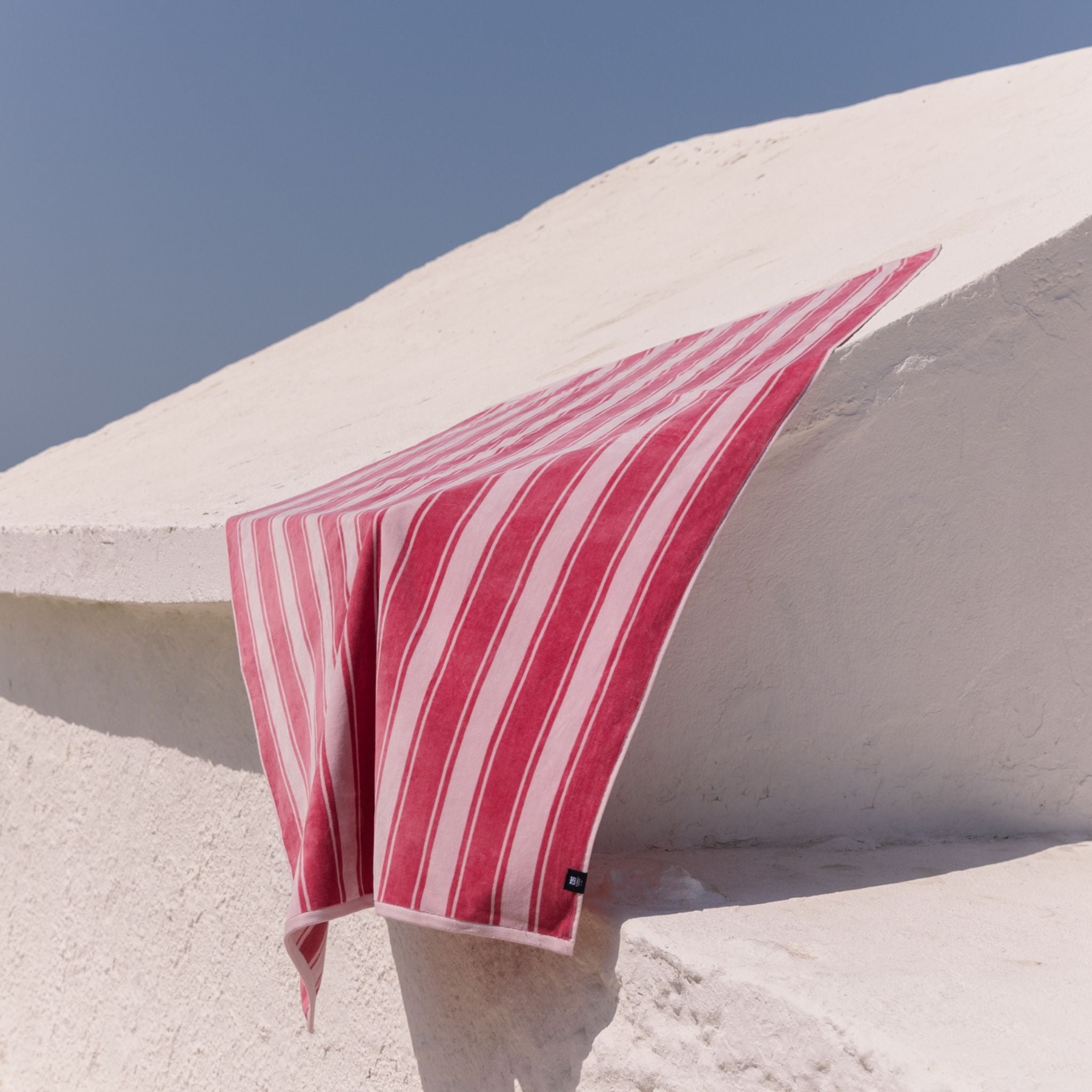 Pink striped beach towel draped over a white architectural structure against a clear blue sky.
