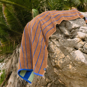 Brown beach towel with blue stripes draped over a stone wall.
