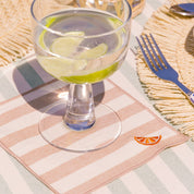 Glass with water and lime slices on a striped tablecloth with a fork and napkin.