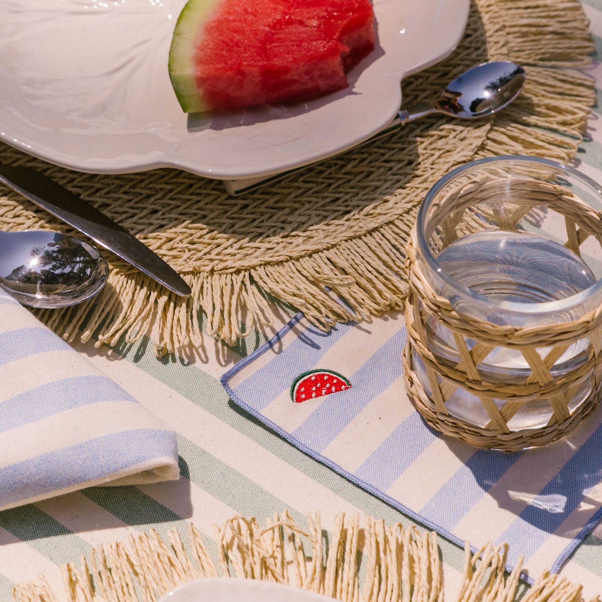 Table setting with watermelon, glass, and striped napkin on a textured tablecloth.
