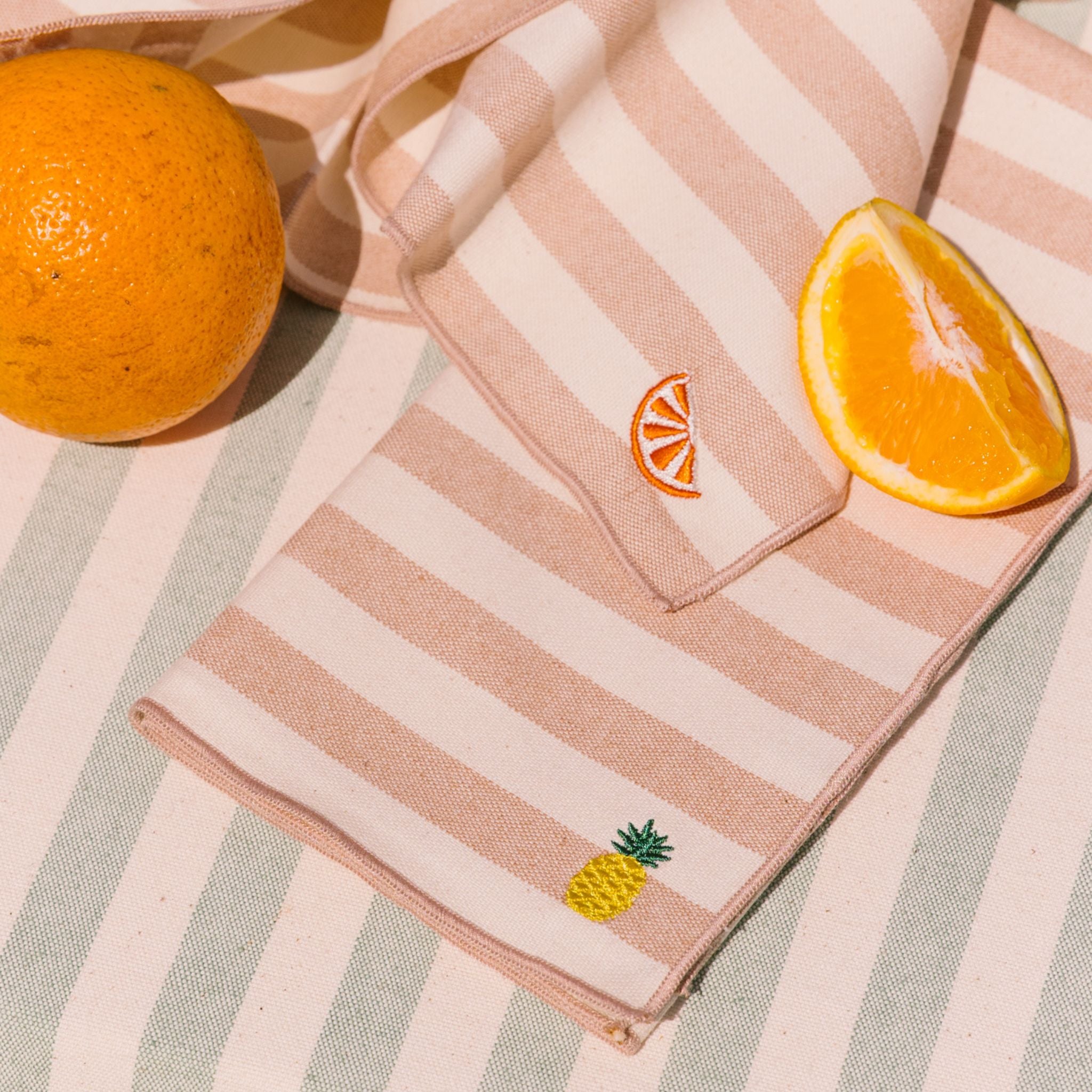 Striped fabric with embroidered designs of an orange and a pineapple, surrounded by oranges on a checkered background.