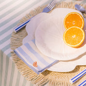 Table setting with white plates, orange slices, and a striped napkin with an orange embroidery on a textured surface.