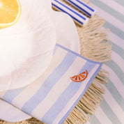 Striped towel with tassels and a orange slice design on a table setting.
