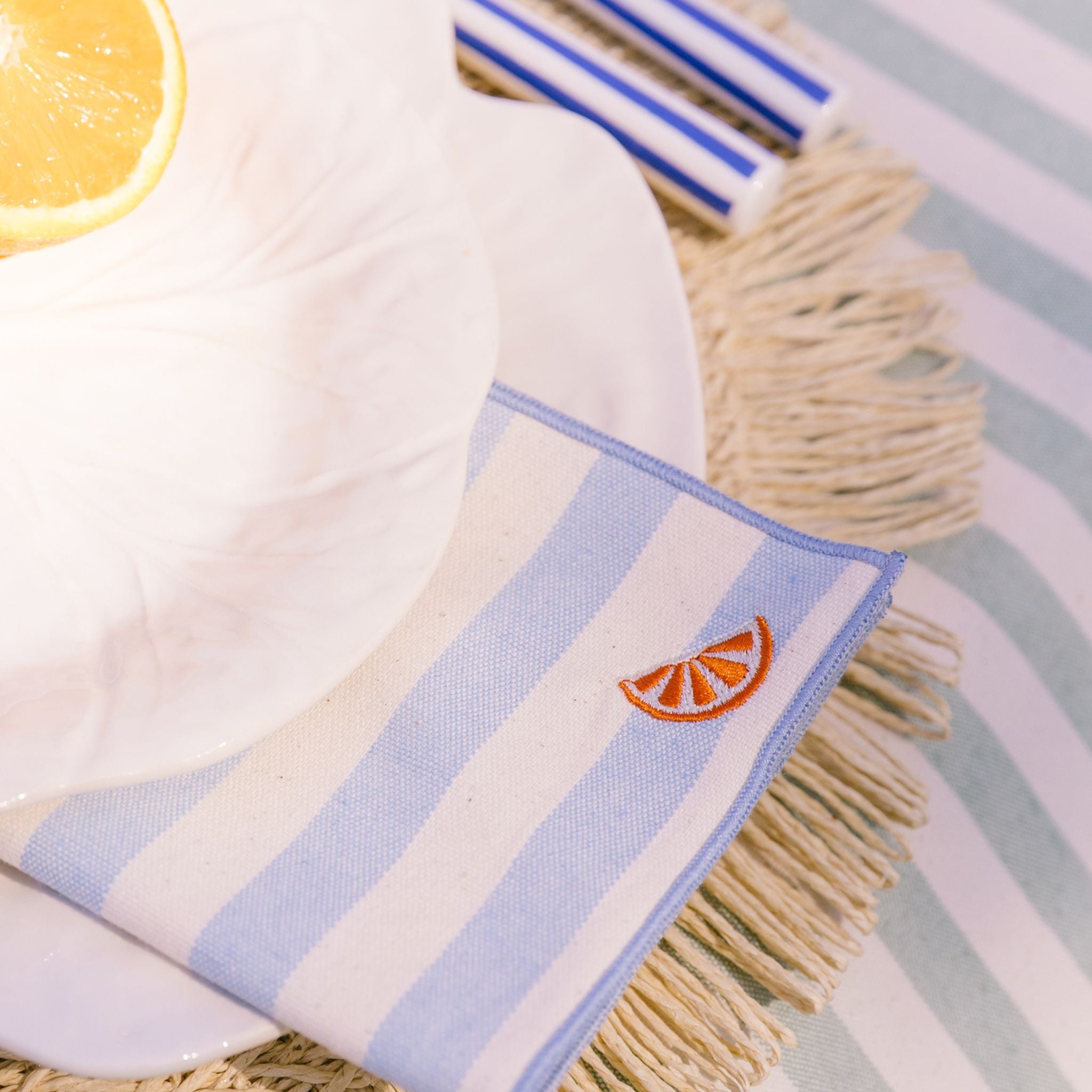 Striped towel with tassels and a orange slice design on a table setting.