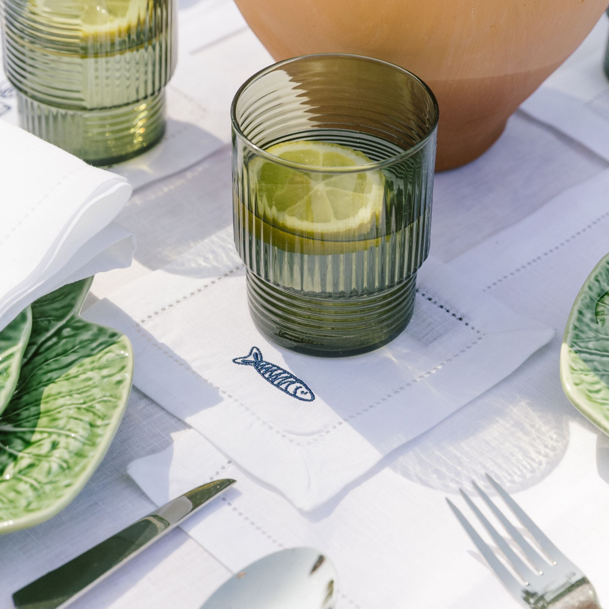 Green glass with lemon slice on a white tablecloth with cutlery.