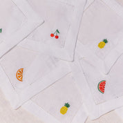 White quilted cocktail napkins with embroidered fruit designs on a beige background