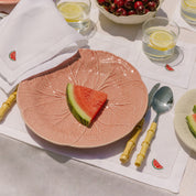 Pink decorative plate with watermelon slice on a table setting with glasses and cutlery.