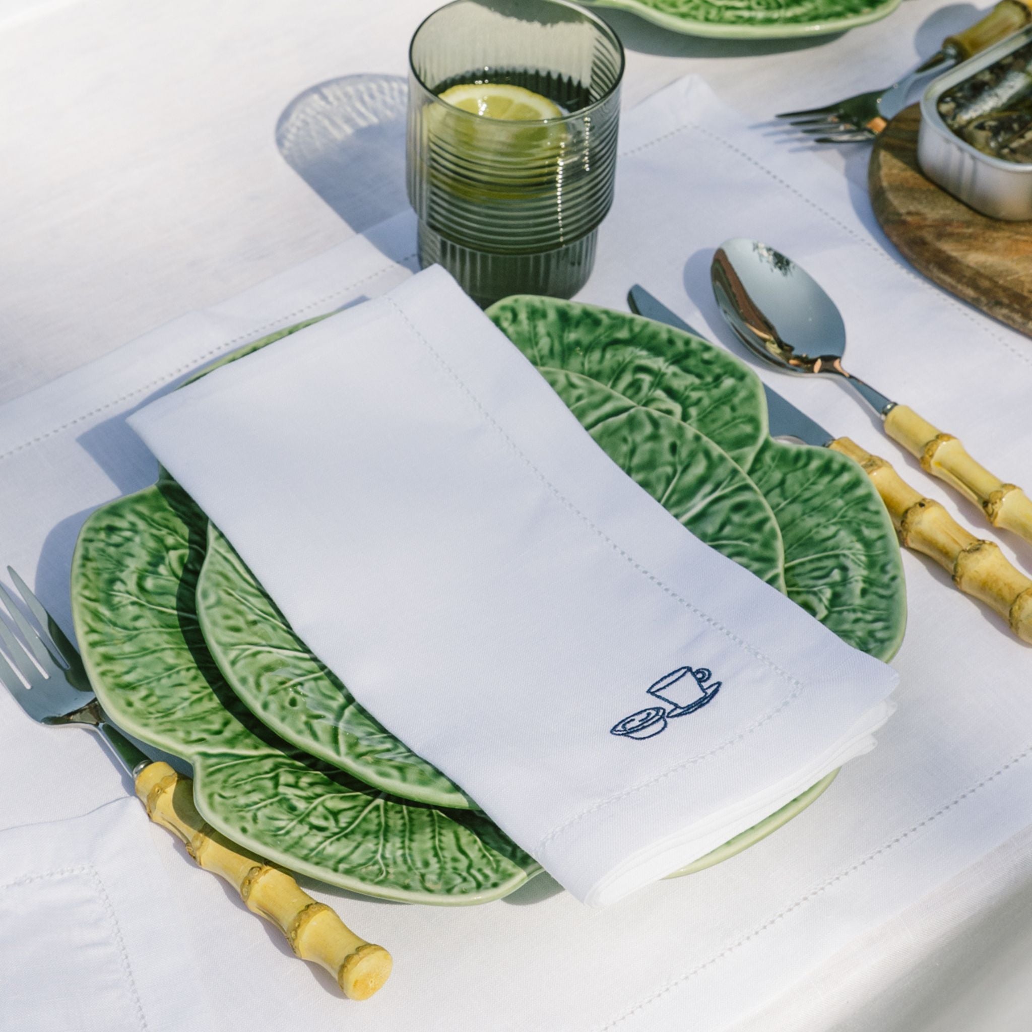 Green ceramic plates with a white napkin featuring a blue embroidery on a white tablecloth.