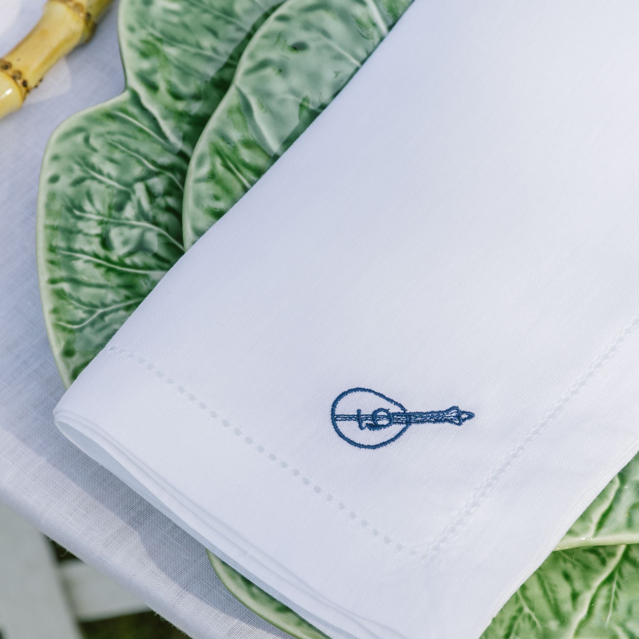 White napkin with a blue embroidered design on green leafy vegetables plate