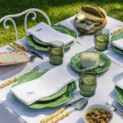 Outdoor dining setup with green plates, glasses, and cutlery on a white tablecloth.