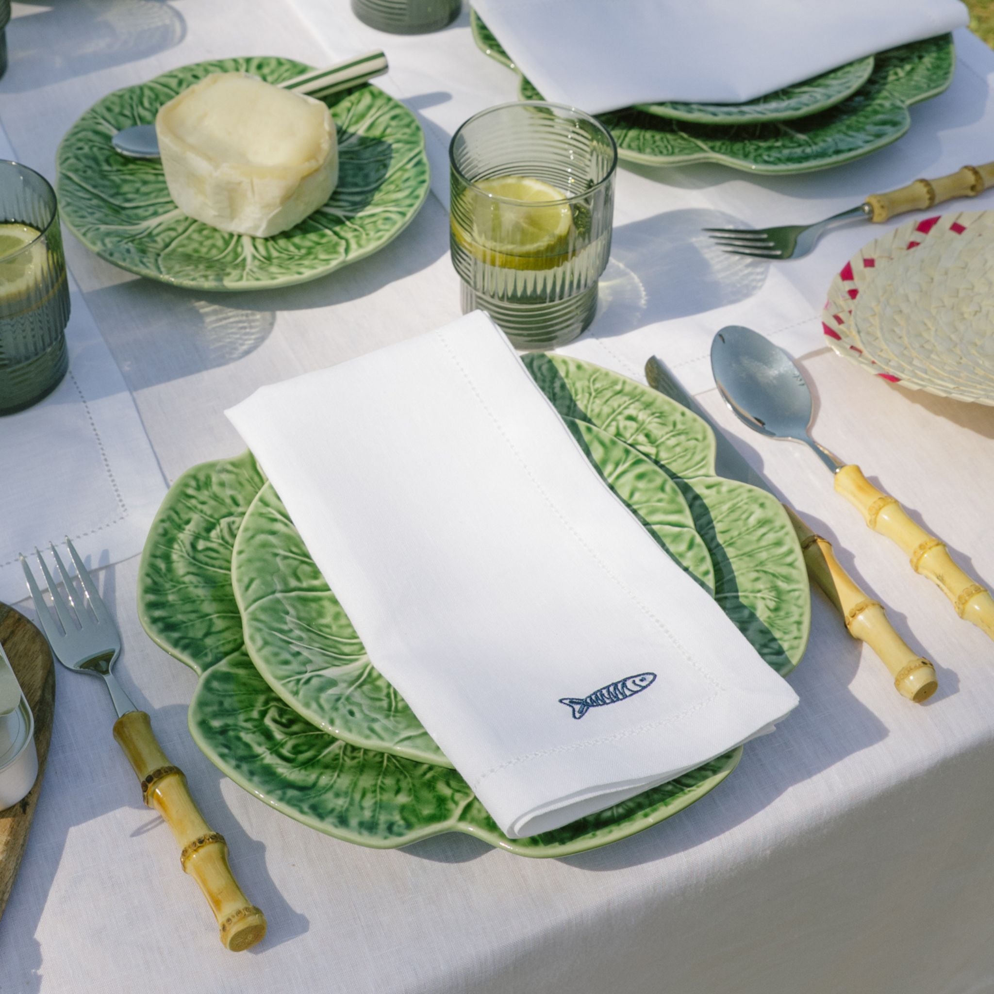Table setting with green ceramic plates, white napkin, and bamboo cutlery on a white tablecloth.